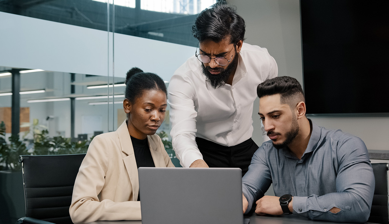 Coloured photograph of three people looking at a laptop