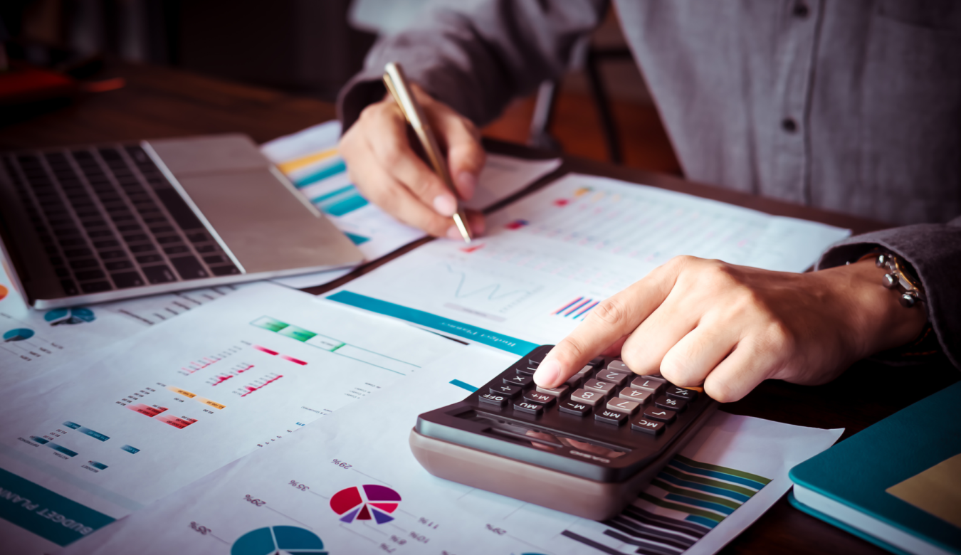 Close up of man's hand typing in numbers on a calculator whilst reviewing business reports