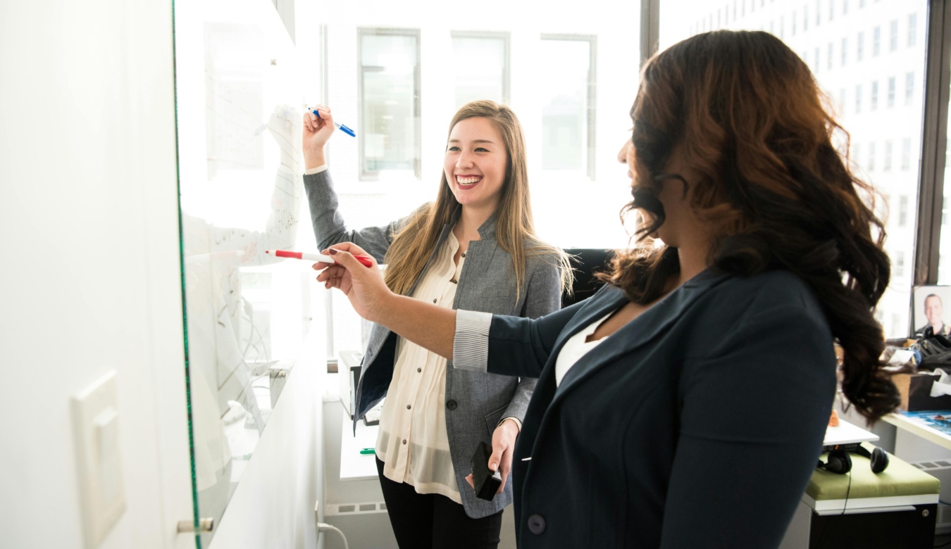 Two women smiling in front of a whiteboard