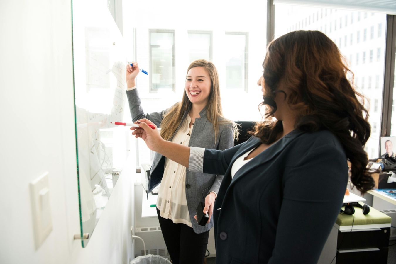 Two women smiling in front of a whiteboard