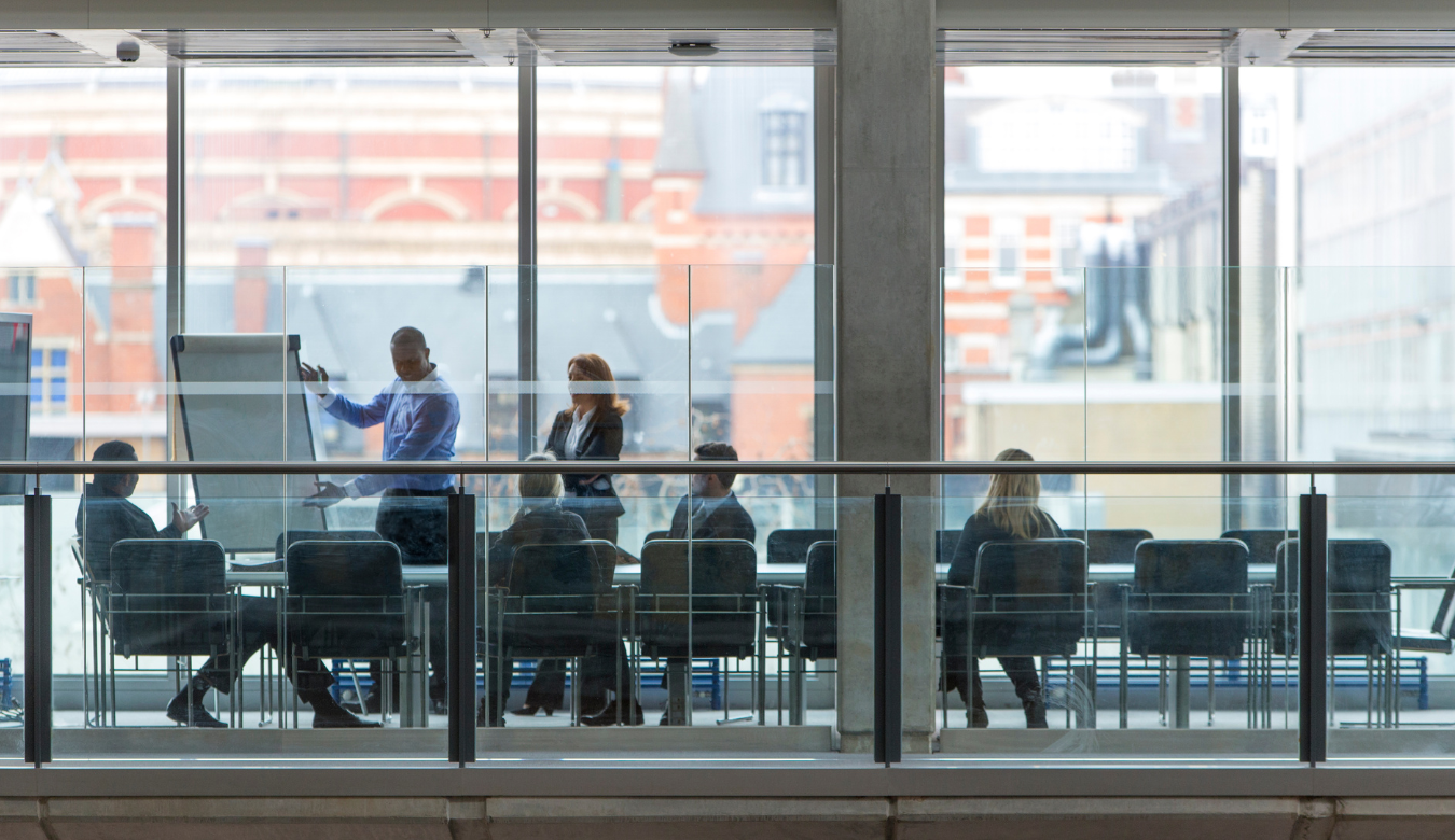 Group of six business people in a boardroom meeting shot at a distance from outside through the glass