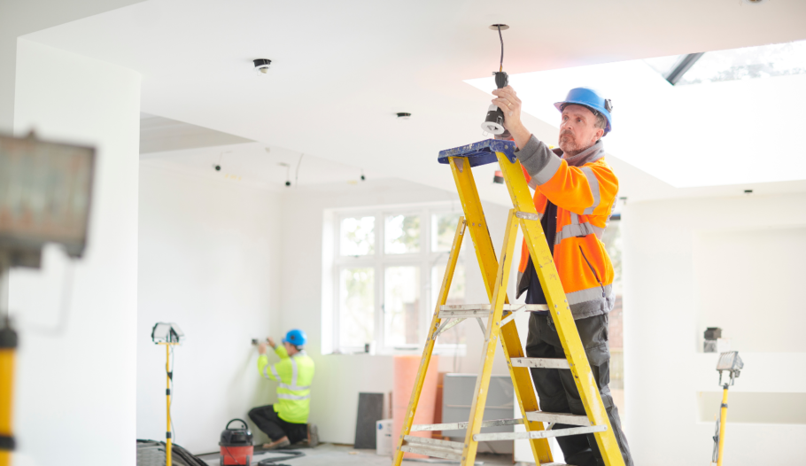 Housing maintenance man in orange hi-vis up a step ladder fixing a light